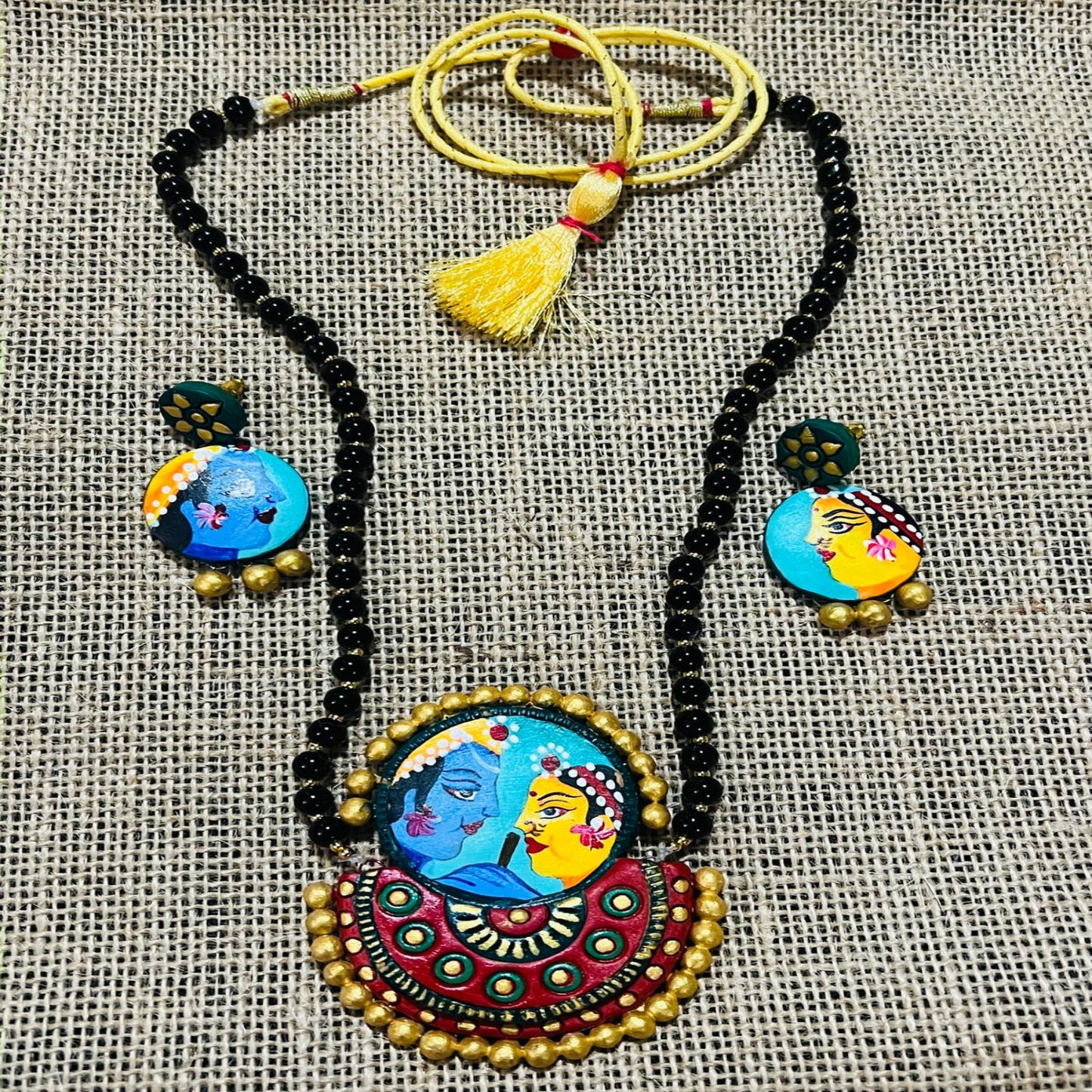 Colorful necklace and earrings set with intricate designs on a textured fabric background