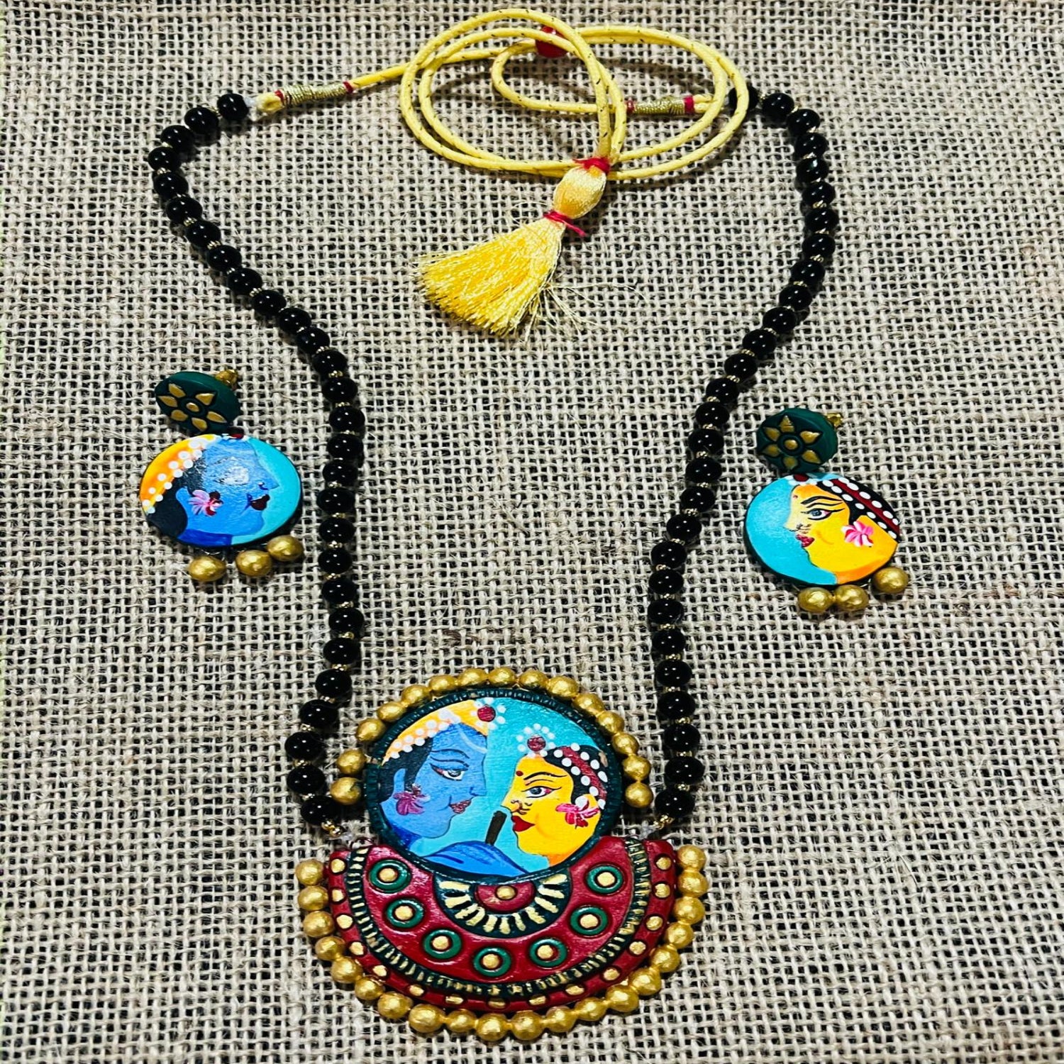 Colorful necklace and earrings set with intricate designs on a textured fabric background